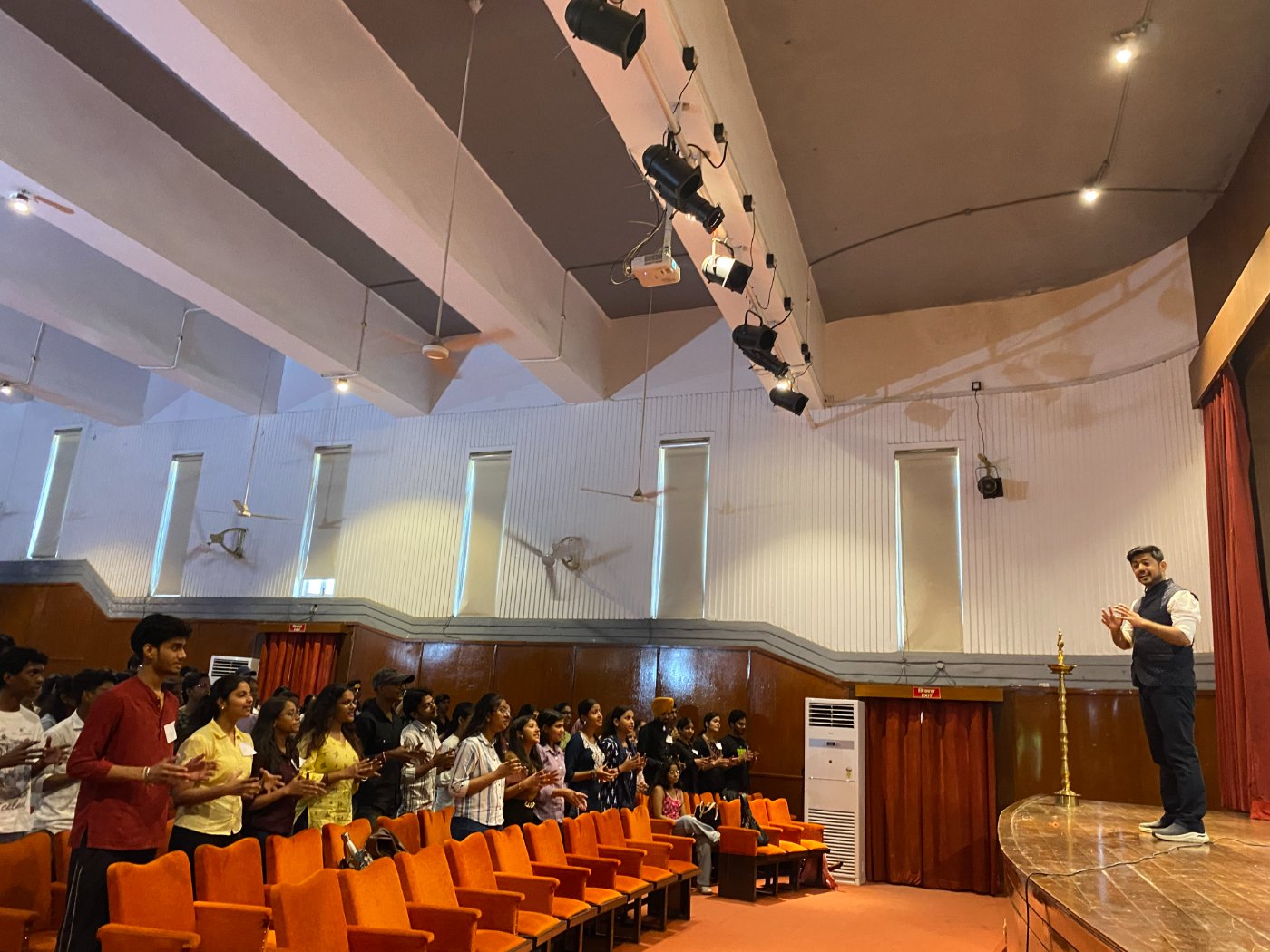 Participants standing and clapping as the facilitator leads a session from the stage