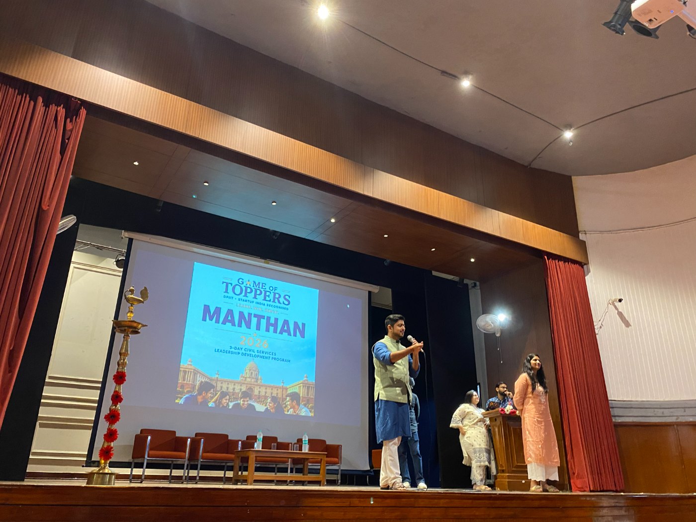 A Manthan facilitator addressing the audience on stage beside the programme screen